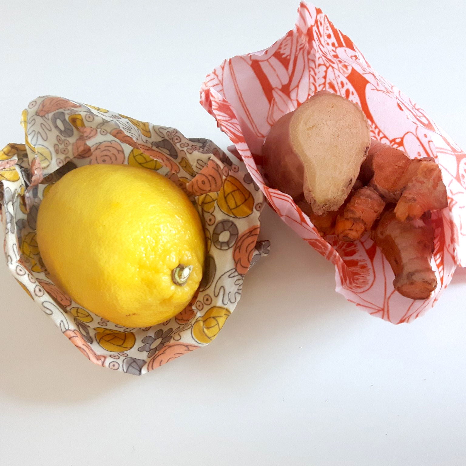 two snack size wax wraps, one holding a lemon, the other holding ginger root