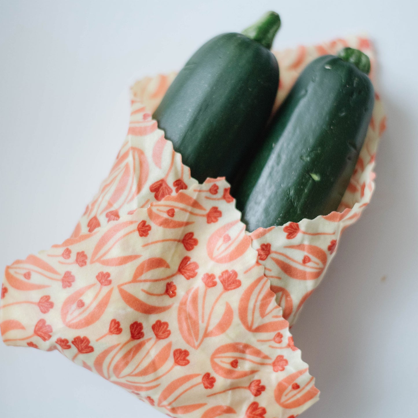 a medium wax food wrap hold two zucchini halves on a white background