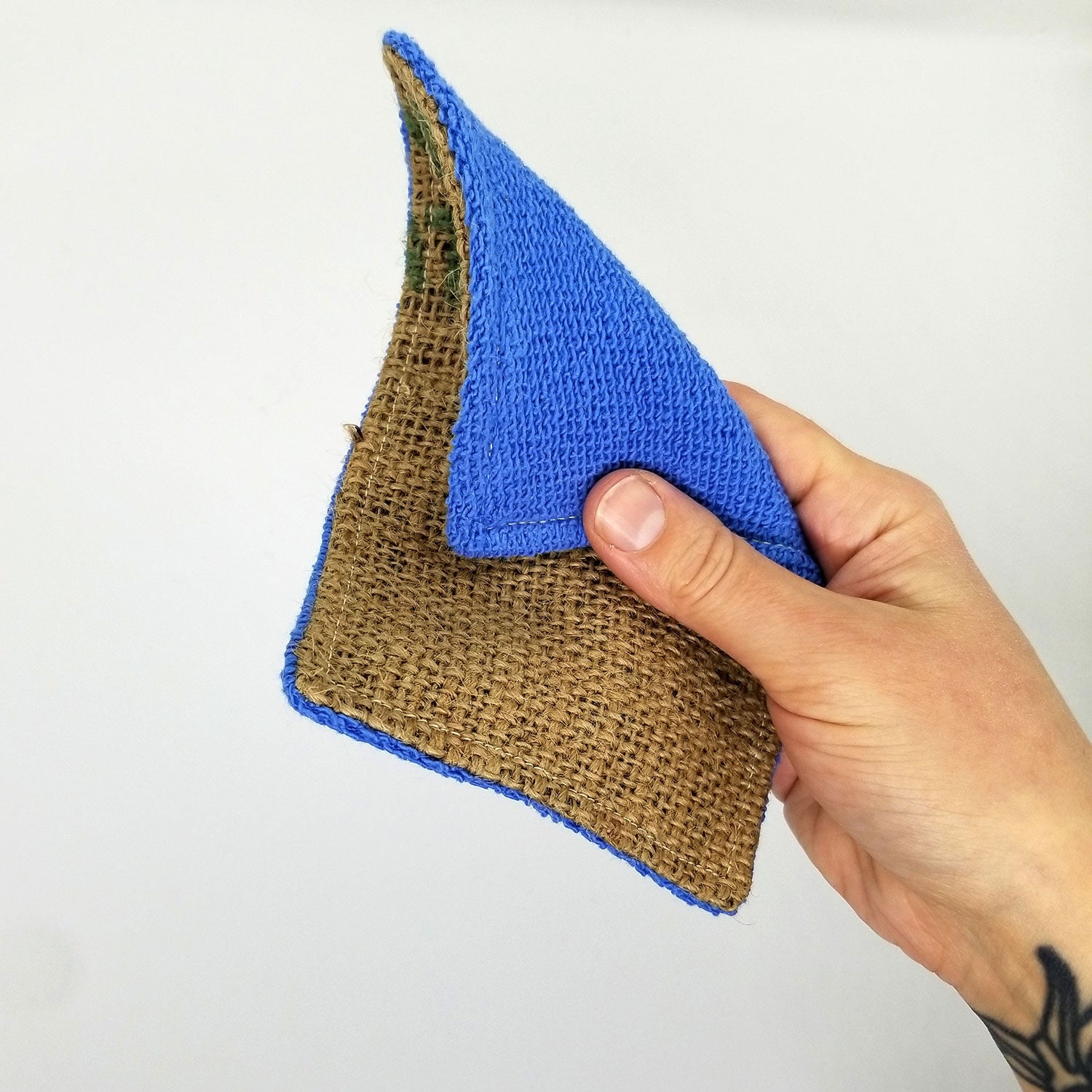 a hand holds up an upcycled dish scrubber, showing both the burlap and terry cloth sides