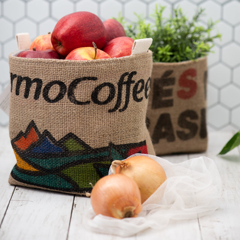 two burlap baskets, one filled with apples and the other with a green plant
